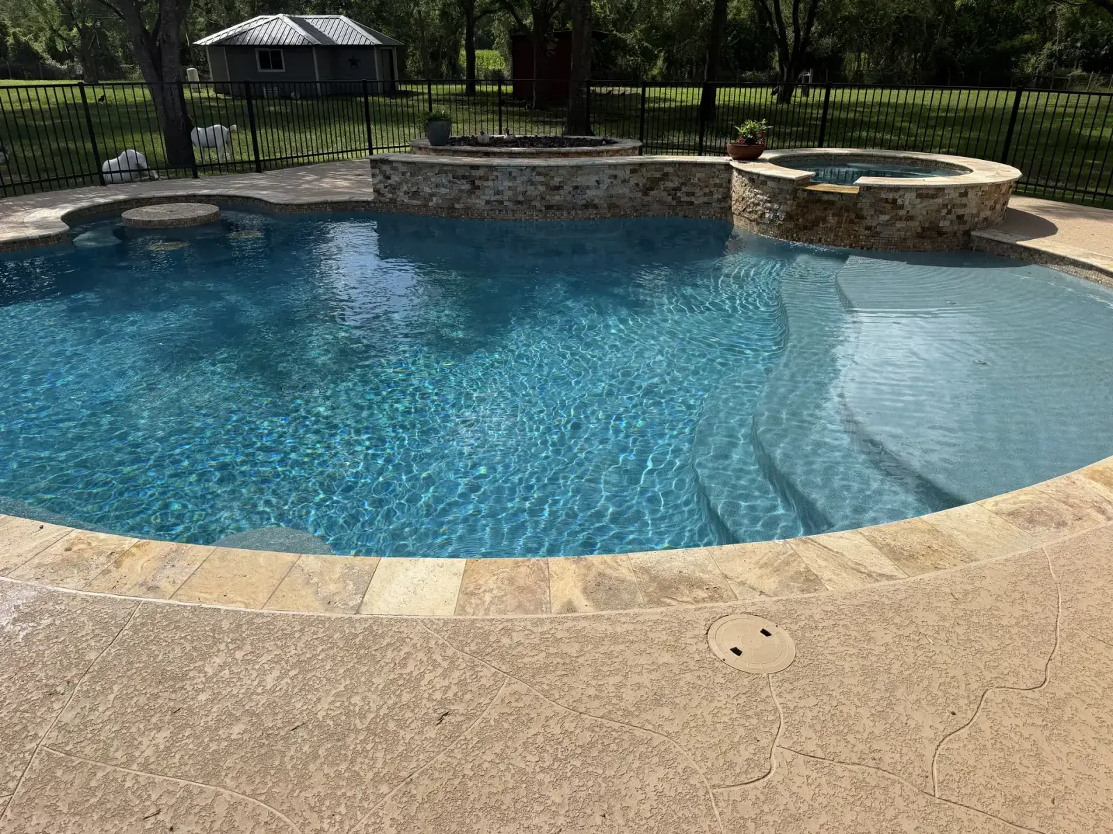 Custom gunite swimming pool with tanning ledge, raised spa, and stone veneer detailing by Venture Pool Company