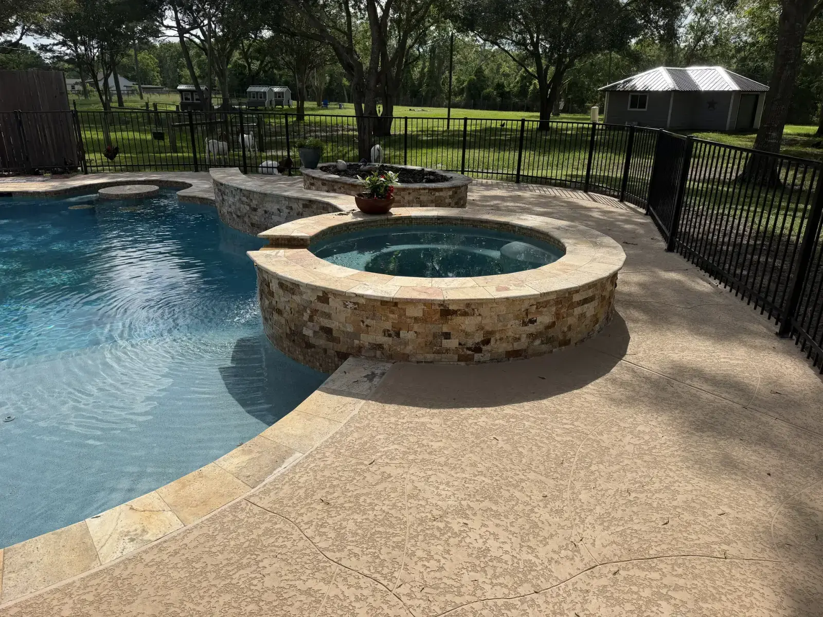 Round raised pool spa featuring stacked-stone veneer and travertine coping, with a stone fire bowl planter