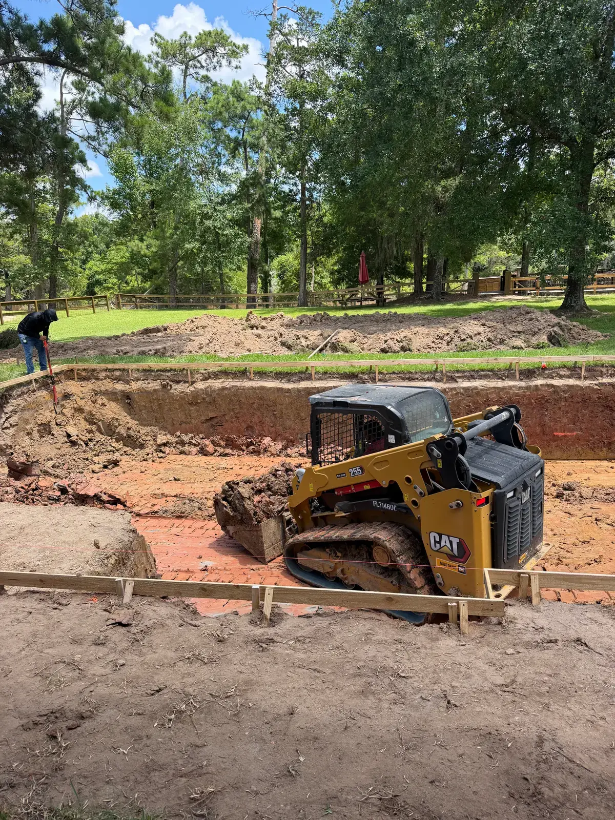 A CAT track loader excavating a new gunite pool as a Venture Pool Company crew member sets the wood form boards